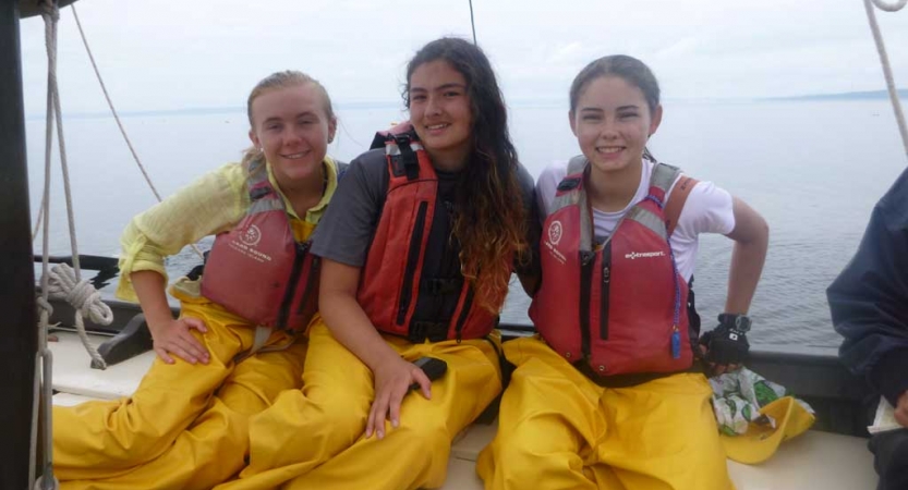 Three people wearing life jackets and rain pants sit on a boat and smile for the photo. 